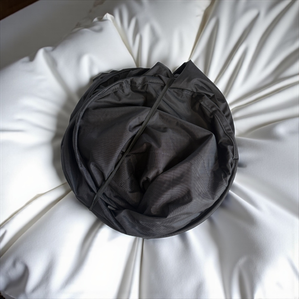Black fabric laundry basket ball on a white sheet bed