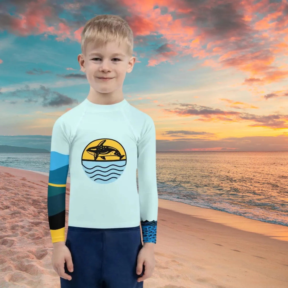 Child wearing a long-sleeve shirt with a dolphin design on a beach at sunset