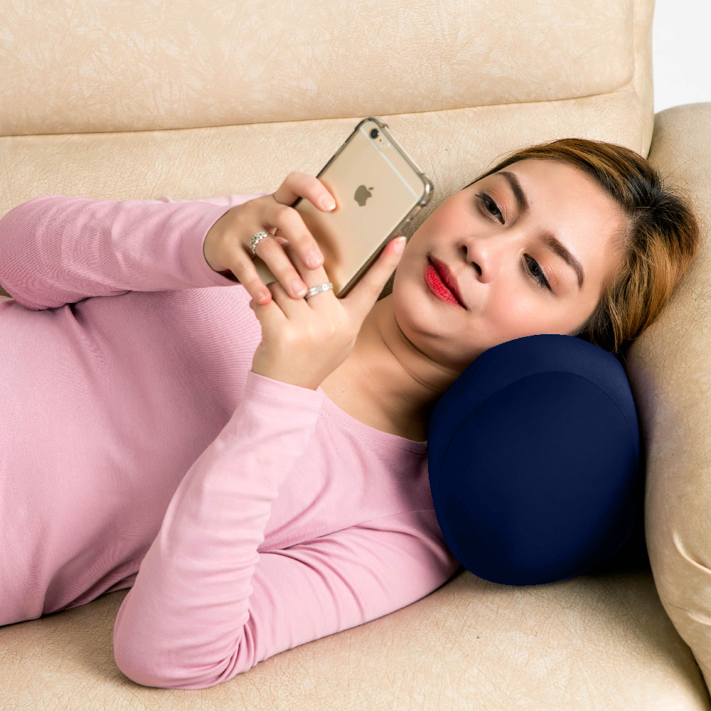Woman lying on a couch with a blue travel pillow and holding a phone.