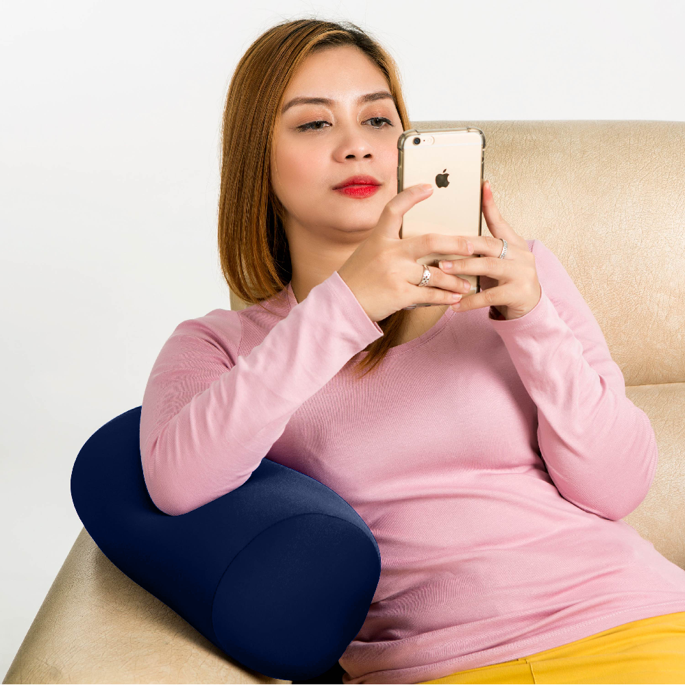 Woman using a blue neck pillow while sitting on a couch and taking a selfie.