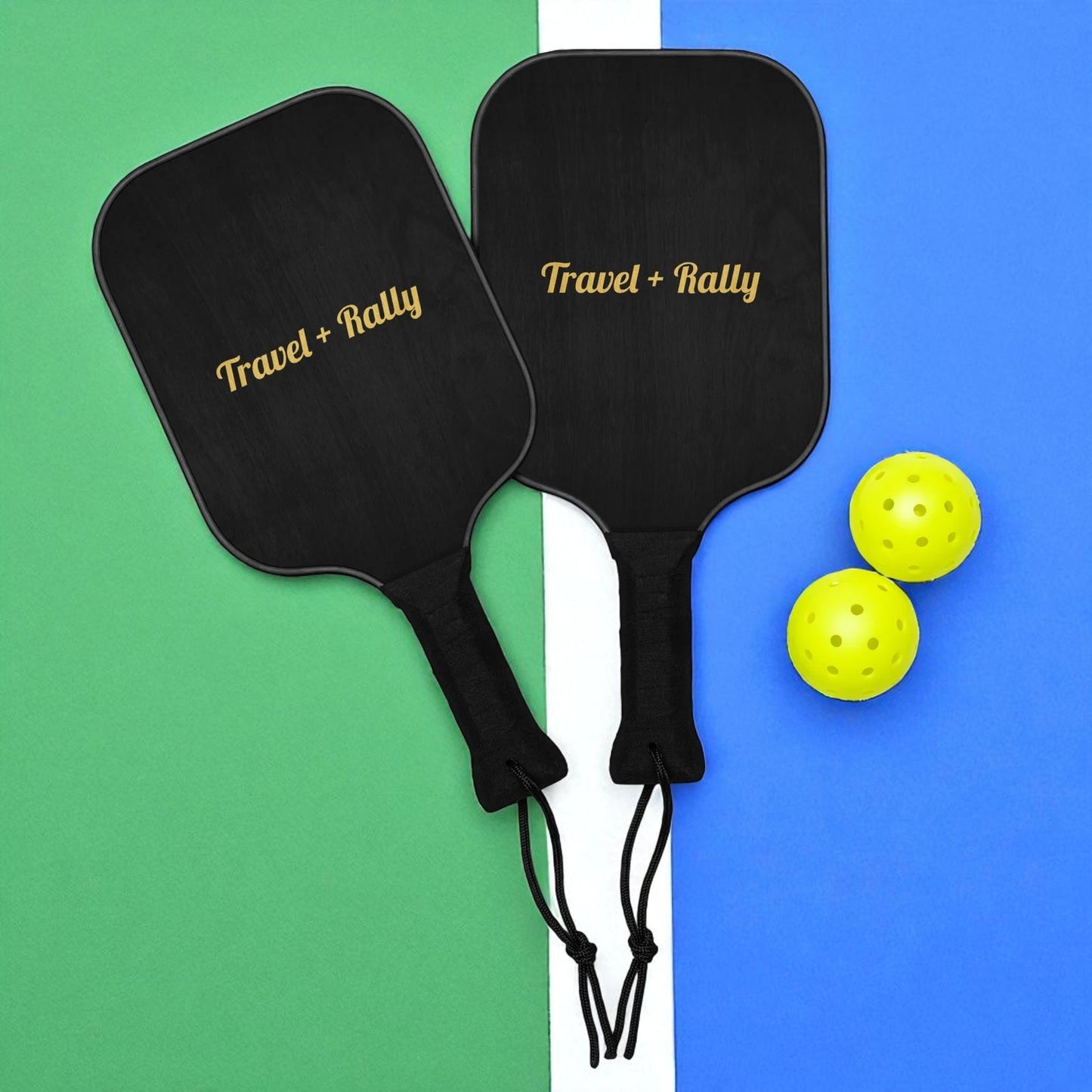 Two black pickleball paddles with 'Travel + Rally' branding on a green and blue background with two yellow pickleballs.