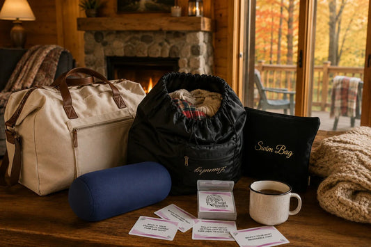 Cozy fall cabin travel essentials including a travel laundry bag, swim bag, mini microbead pillow, and National Parks card game on a cabin table near a fireplace