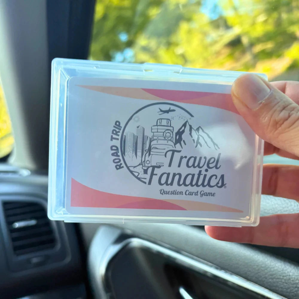 Hand holding a 'Travel Fanatics' card game box inside a car.

