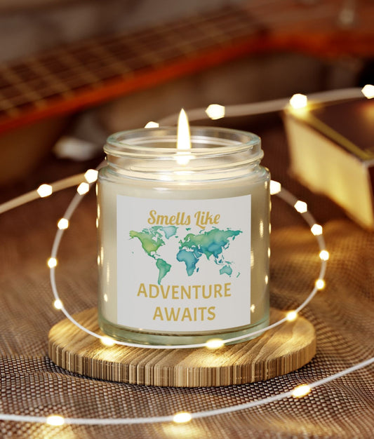 Candle in a jar with 'Adventure Awaits' label on a wooden coaster surrounded by string lights, with a guitar in the background.

