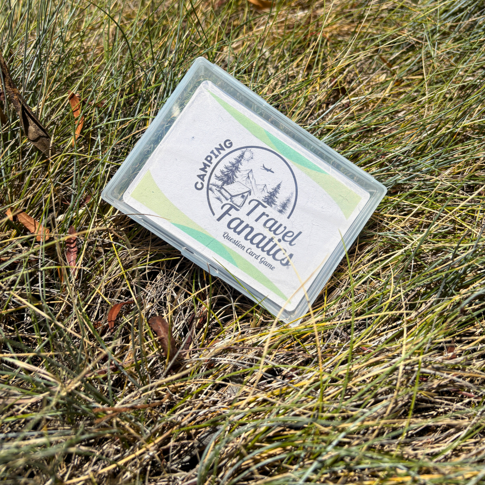 perfect game box labeled 'Camping Travel Fanatics' on grass perfect for camping trips, Card game packaging with text about camping conversations and questions for ages 14 and up.