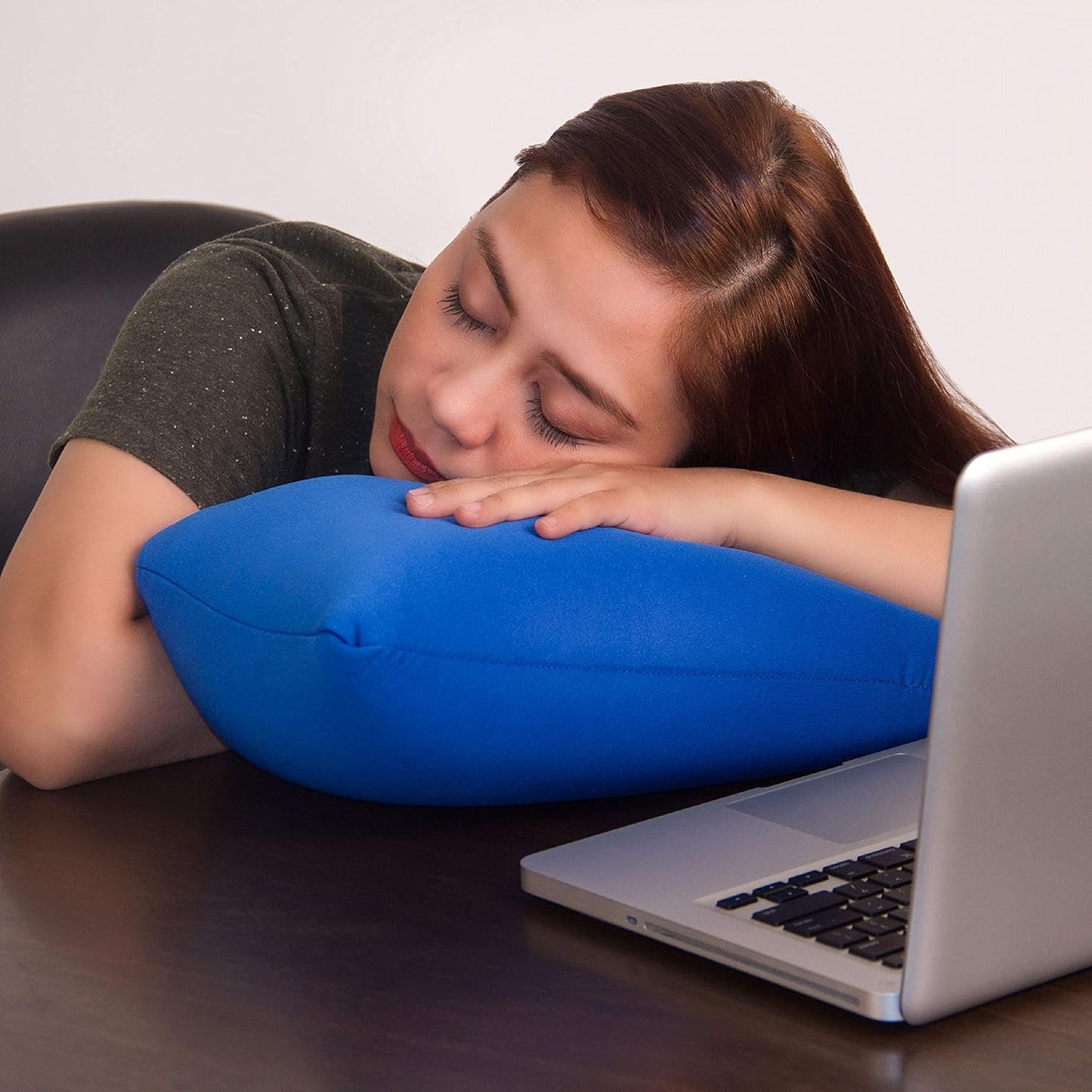 Person using a blue pillow for support while lying on a desk with a laptop.

