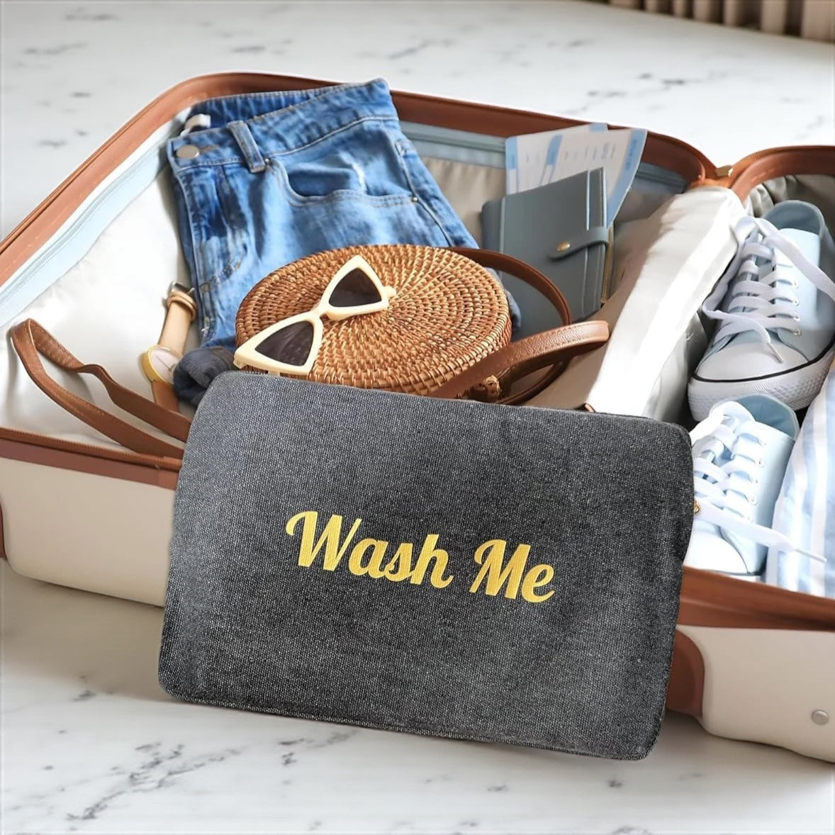Gray pouch with 'Wash Me' text in a suitcase with clothes and accessories.

