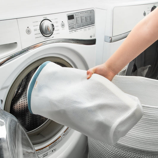 Person using a laundry bag to load clothes into a washing machine

