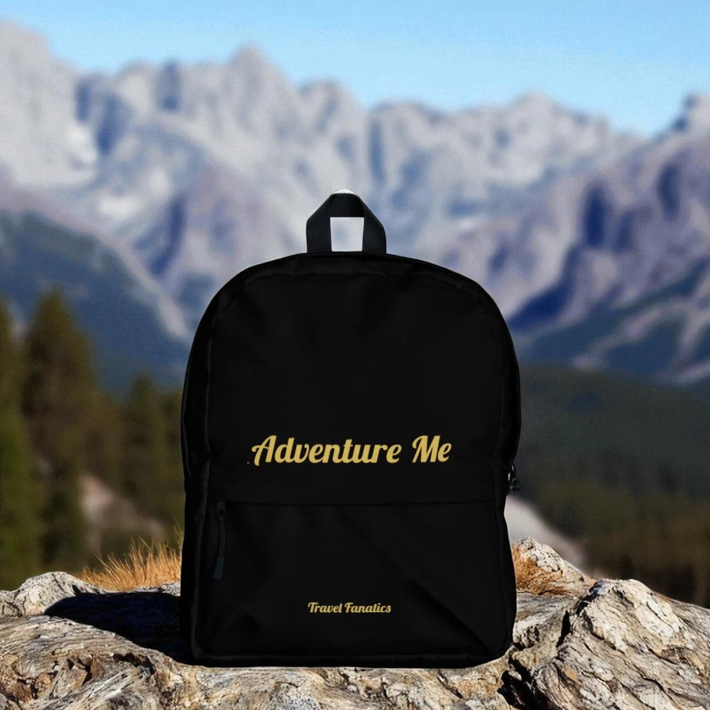 Black backpack with 'Adventure Me' text on a rock with mountains in the background

