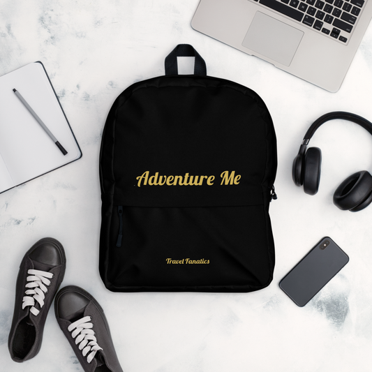 Black backpack with 'Adventure Me' text on a white surface with accessories.

