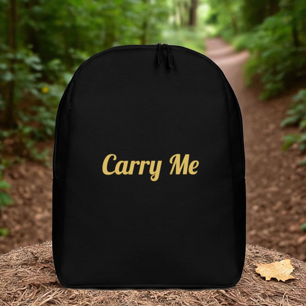 Black backpack with 'Carry Me' text in gold on a forest floor background

