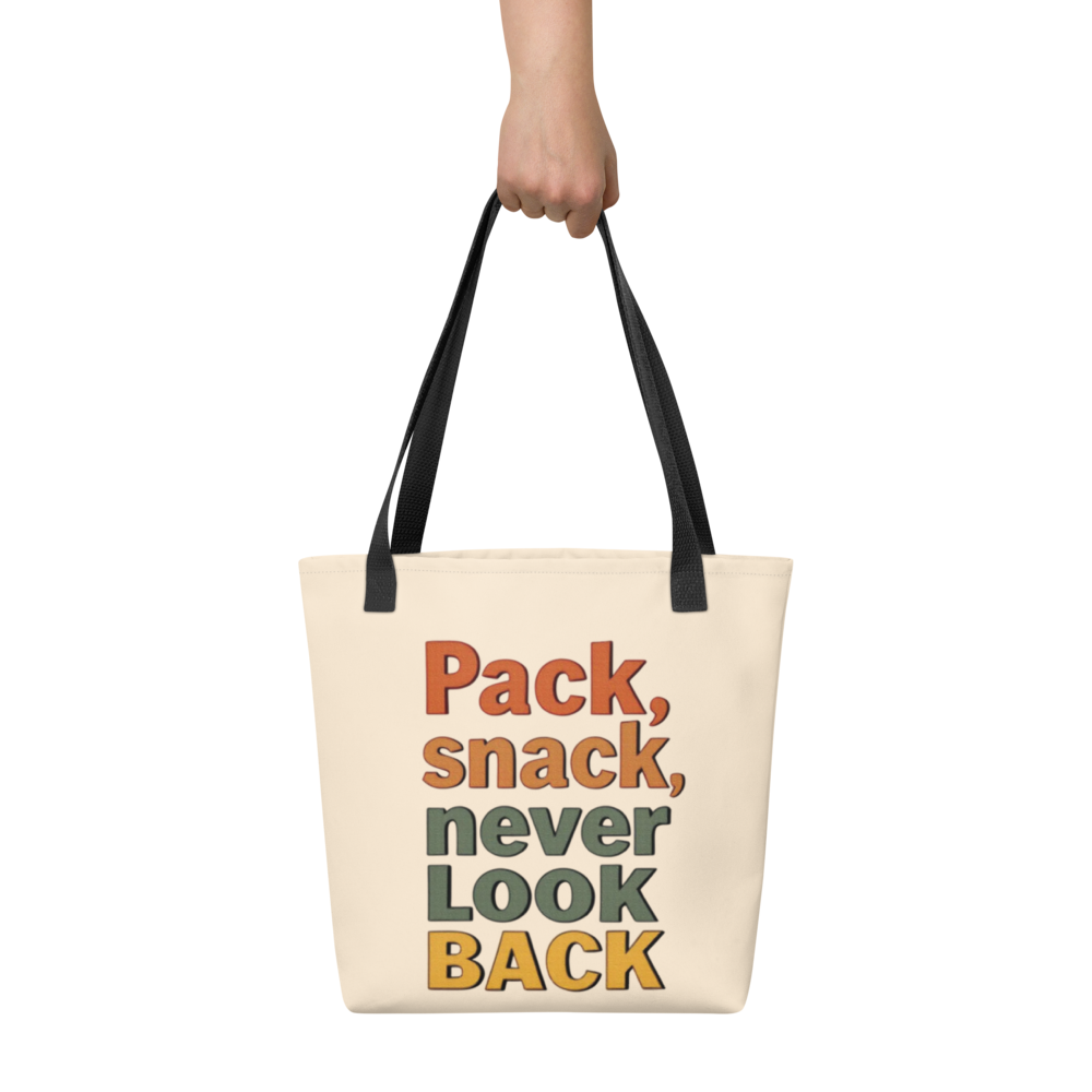 Beige tote bag with colorful text 'Pack, snack, never look back' held by a hand on a white background

