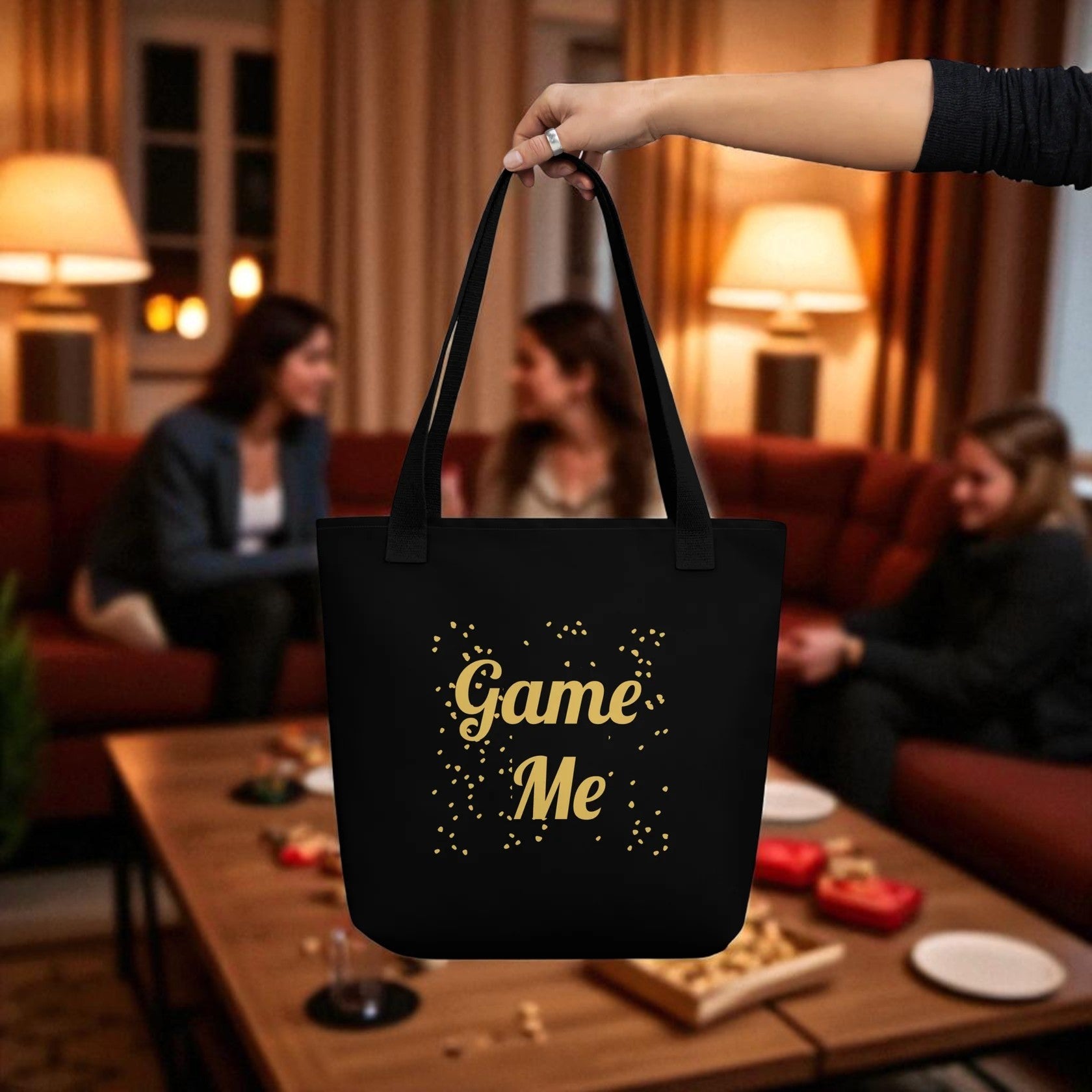 Black tote bag with 'Game Me' text held by a hand in a social setting.

