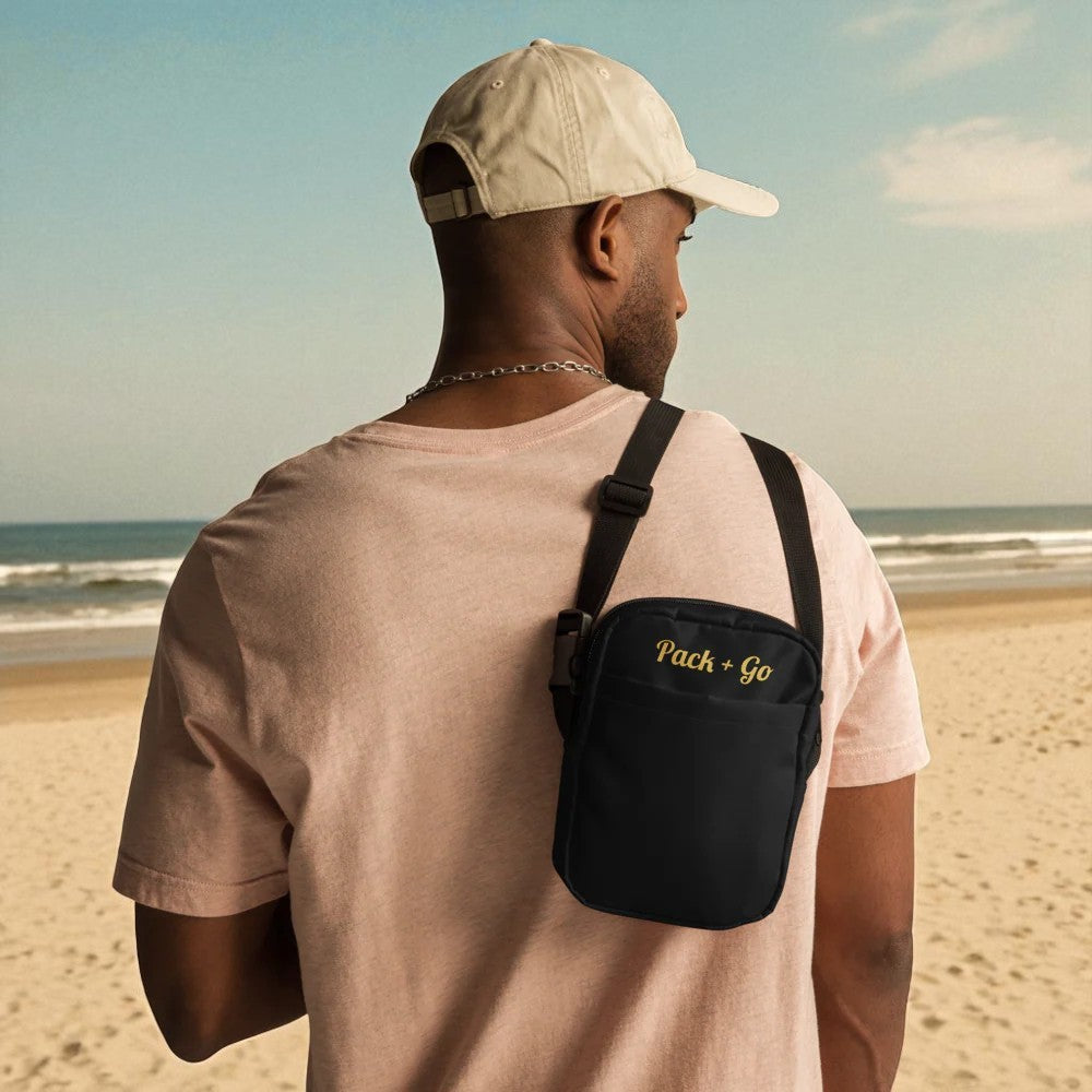 Man on a beach wearing a beige cap and carrying a black 'Pack & Go' bag.

