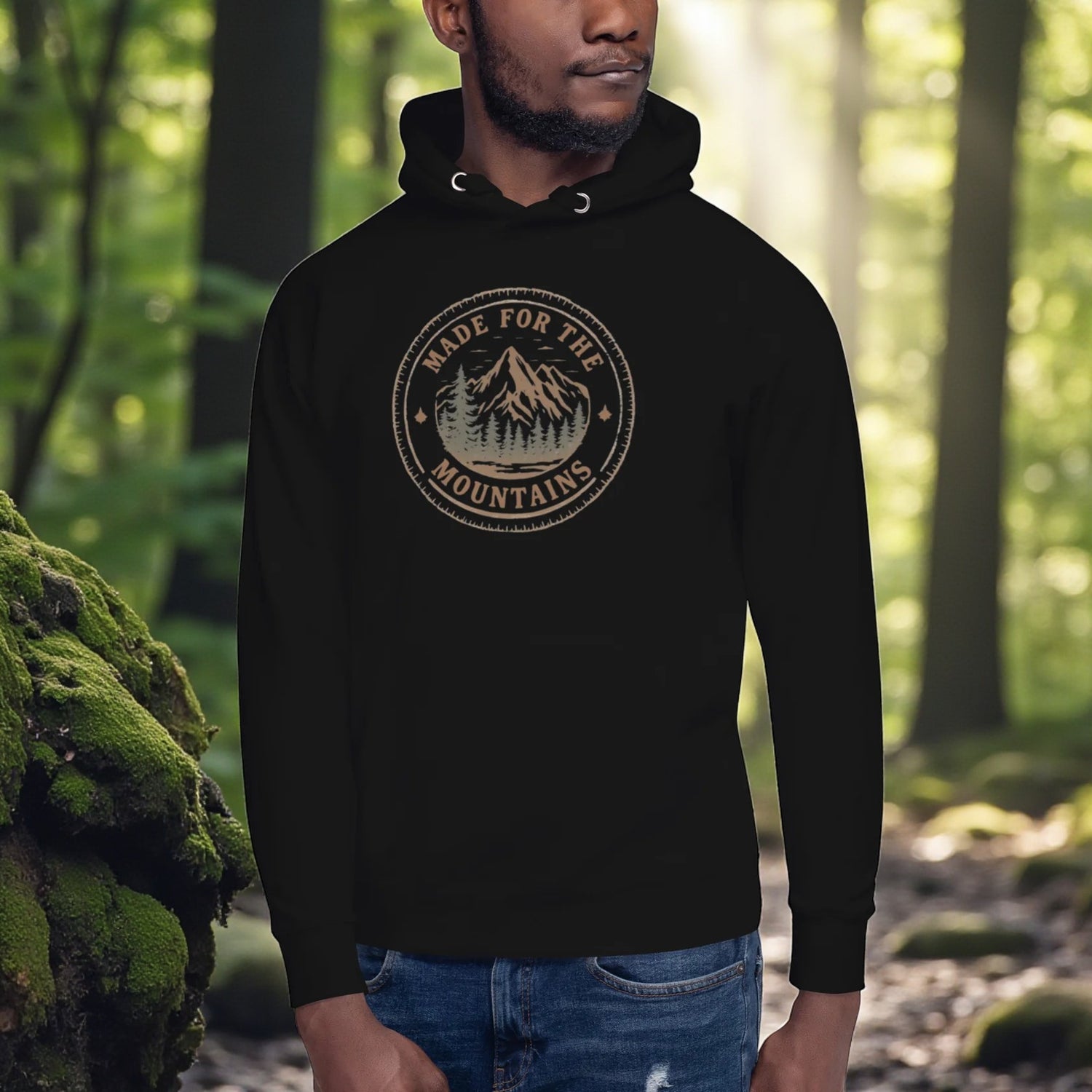 Person wearing a black hoodie with a mountain logo in a forest setting

