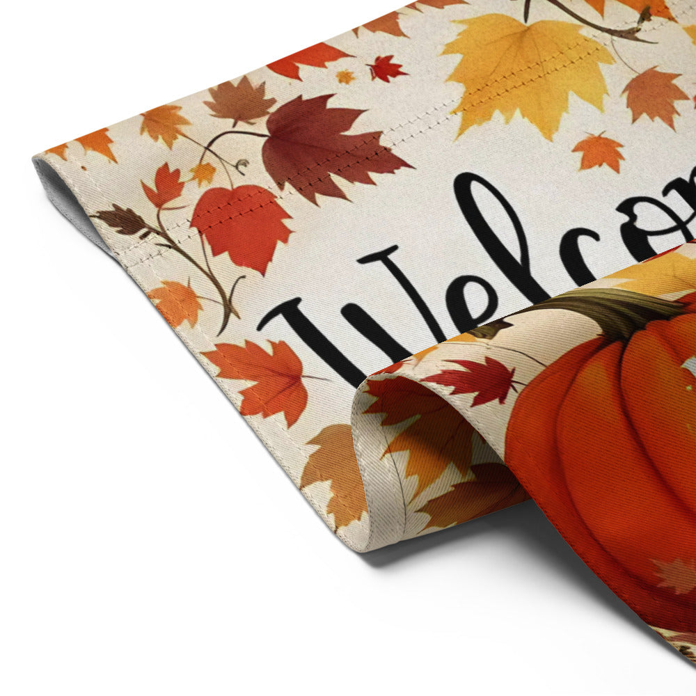 Decorative table runner with autumn leaf pattern and 'Welcome' text, next to a pumpkin.

