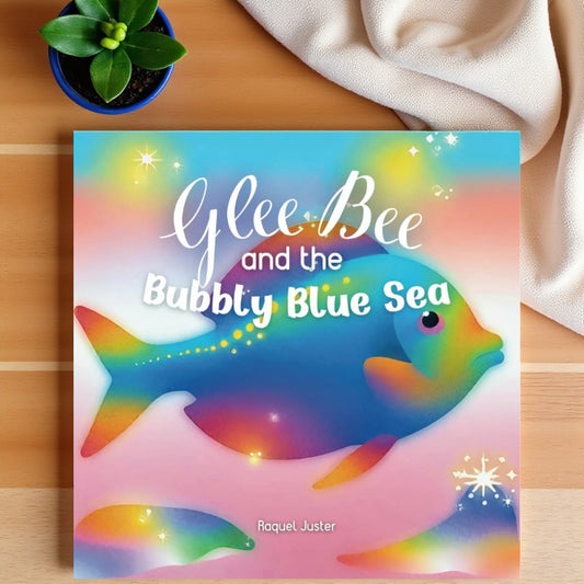 Book titled 'Glee Bee and the Bubbly Blue Sea' with a colorful fish illustration on a wooden surface.

