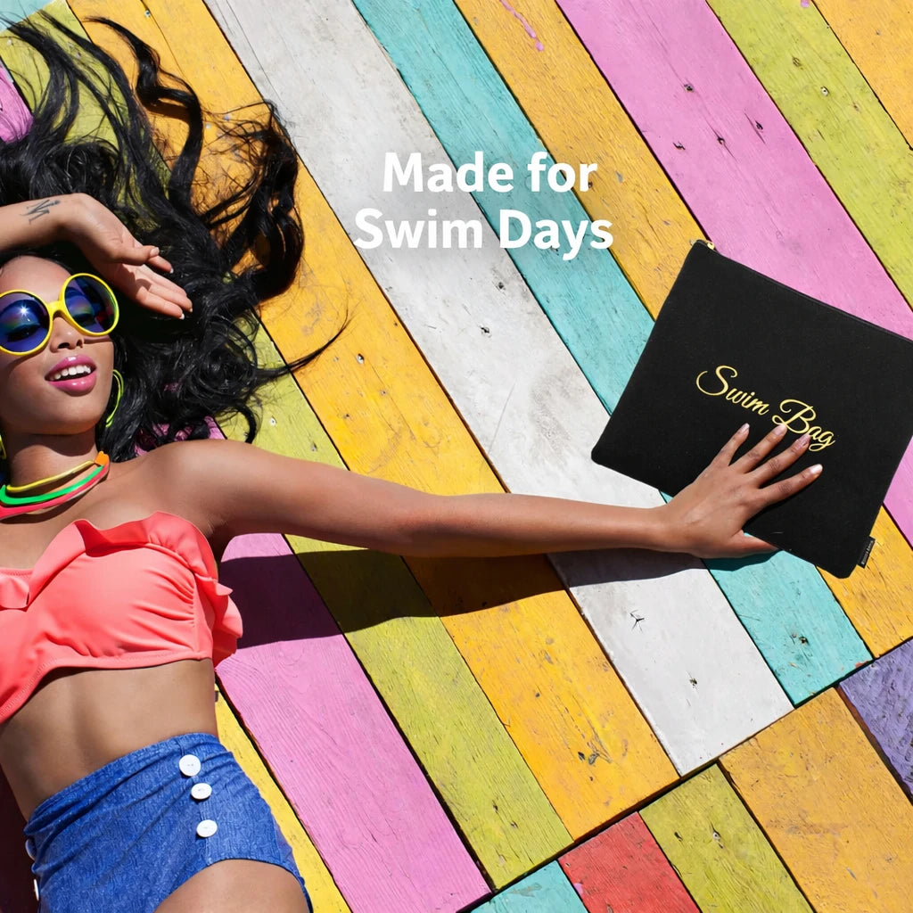 Woman relaxing on a colorful deck holding a black waterproof swim bag with gold lettering, designed for beach and swim days.