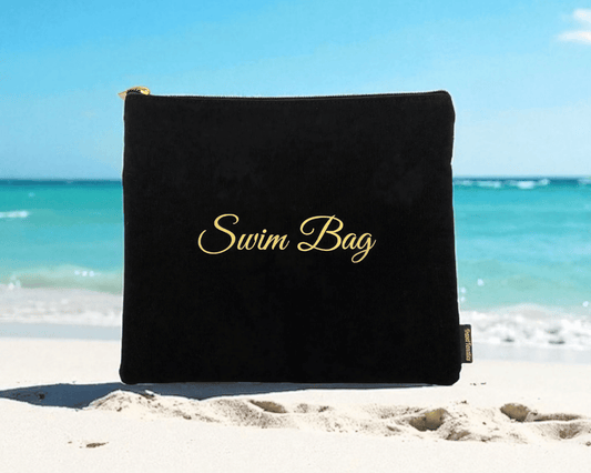 Black swim bag with 'Swim Bag' text on a sandy beach with ocean in the background

