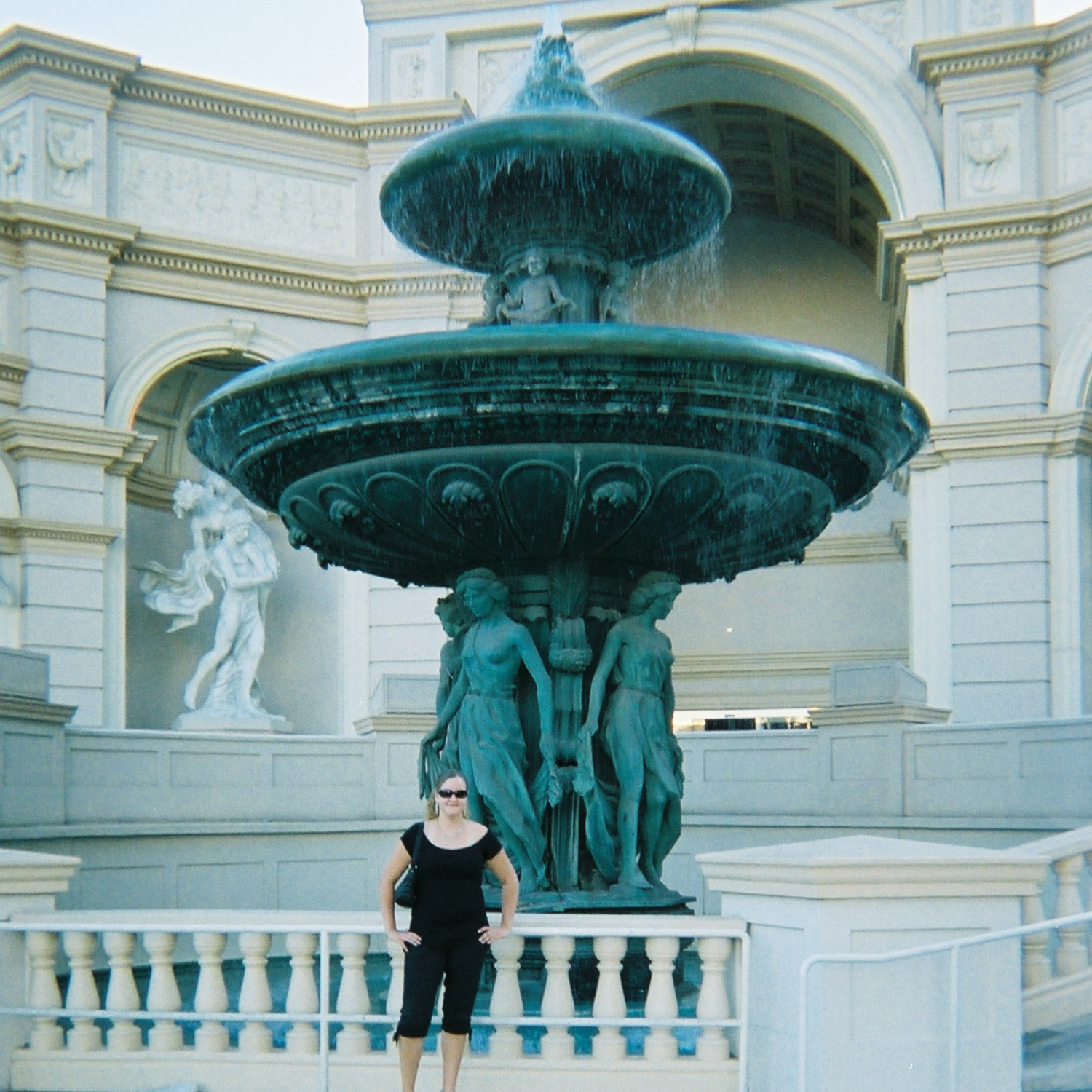 Woman standing in front of a large ornate fountain with classical sculptures.

