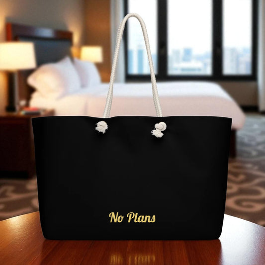 Black tote bag with 'No Plans' text on a table in a bedroom setting

