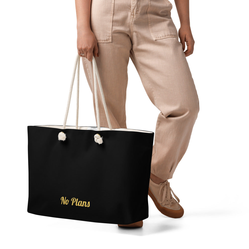 Person holding a black tote bag with 'No Plans' text on a white background